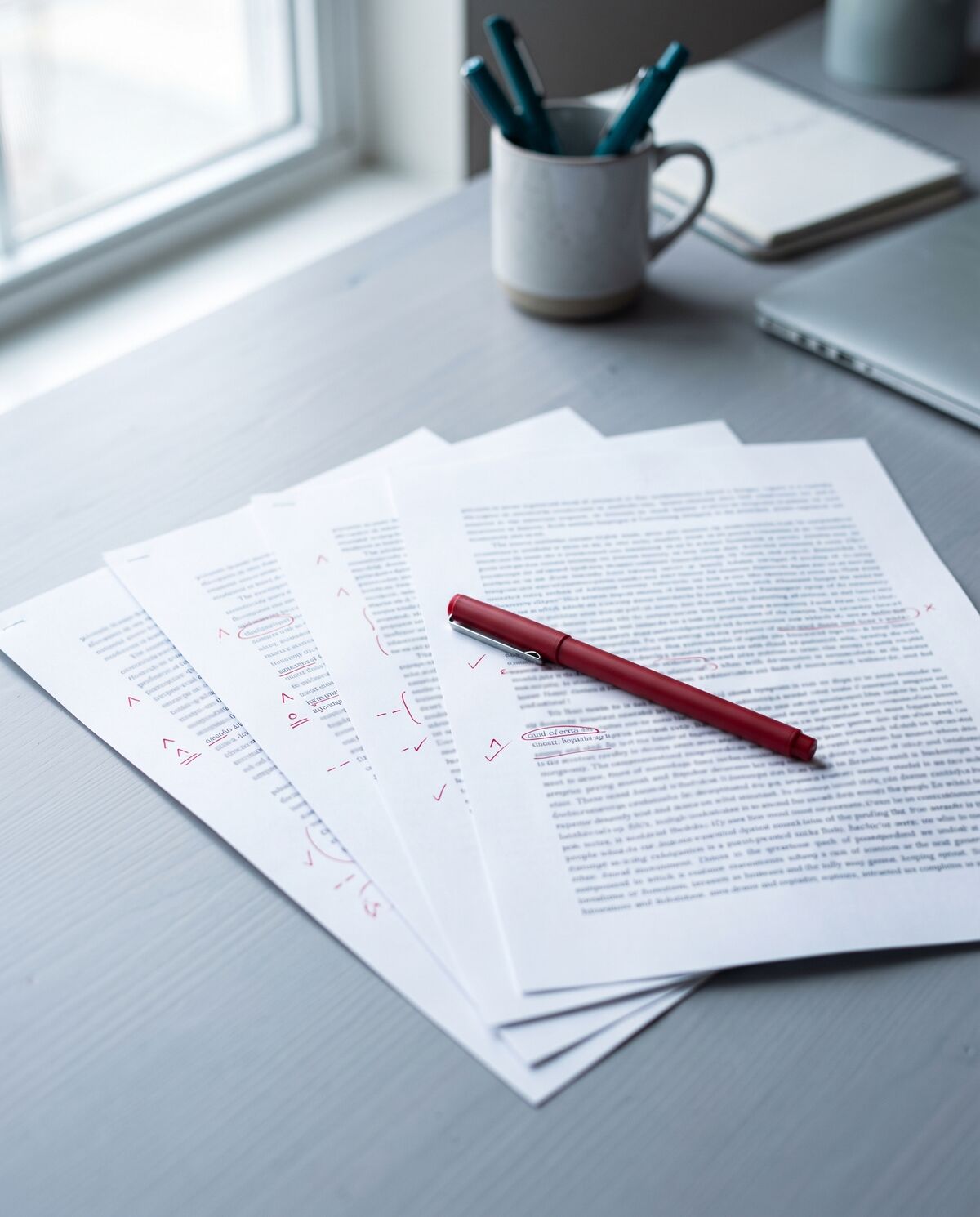 Printed manuscript pages marked up with red proofreading symbols, a red pen resting across them